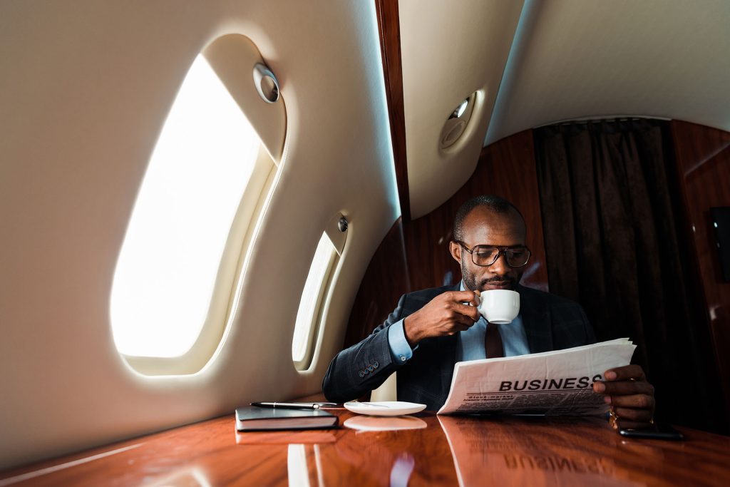 American businessman reading business newspaper while drinking coffee in private plane