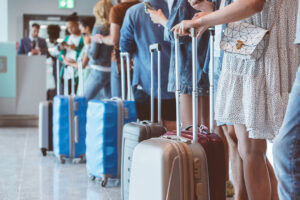 Travelers with luggage using smart phones while waiting in line for boarding at airport