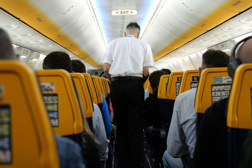 Male flight attendant walks along aisle offering help to Ryanair airplane passengers | Photo: ShowRecMedia / Shutterstock.com