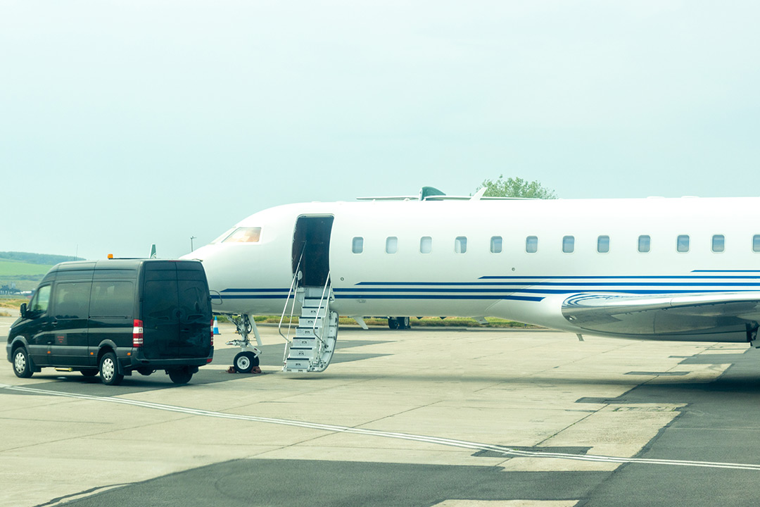 Private jet parked on airport tarmac with luxury ground transportation van beside aircraft