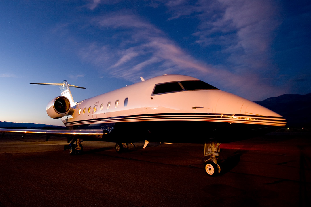 Large private jet parked on runway at sunset with runway lights illuminated
