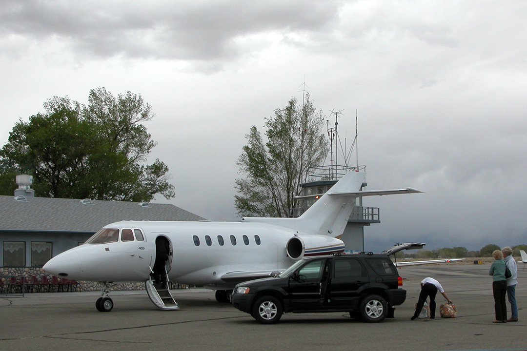 Small private jet parked at regional airport with SUV and passengers nearby