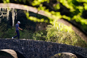 A single golfer walks across the stone bridge over Rae's Creek. | Photo: masters.com
