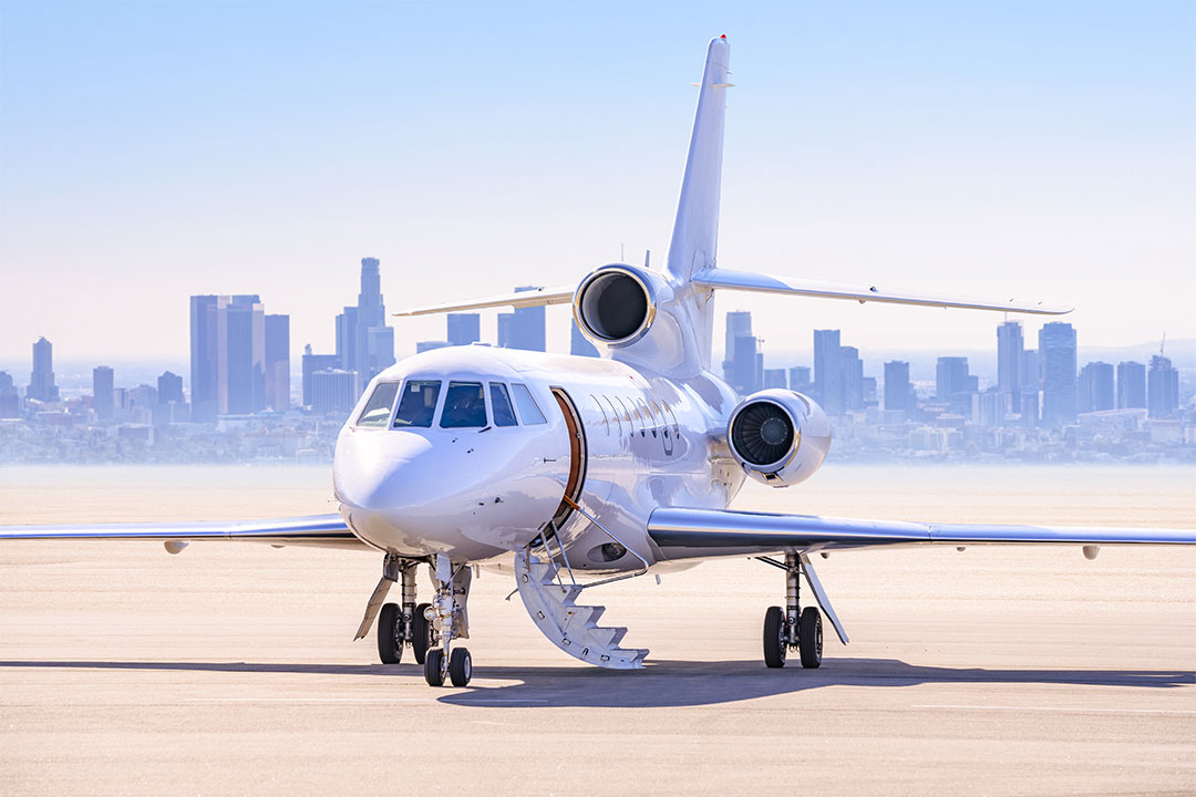 A private jet sits on the tarmac with city of Los Angeles in the distance.